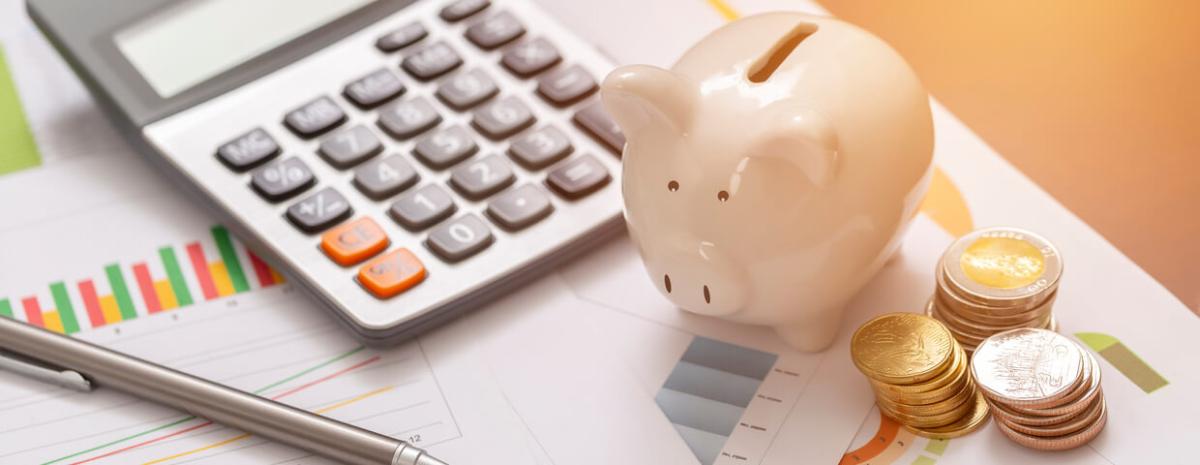 Piggy bank on top of papers next to coins, a pen, and a calculator 