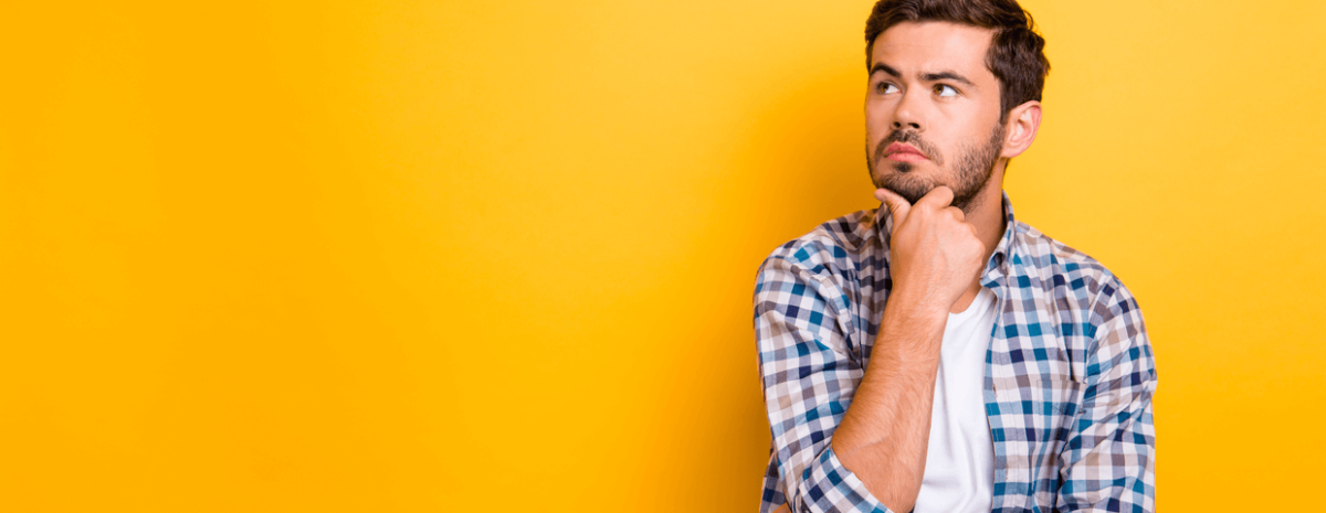 Close up portrait of thoughtful man who looks away touching his chin in front of yellow wall