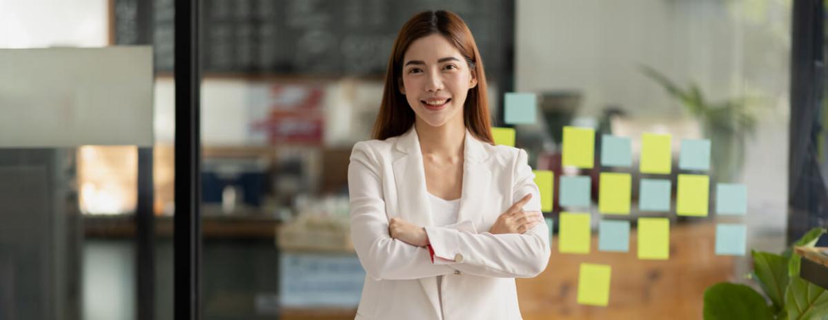 A woman smiling with arms crossed, standing in front of window with sticky notes on it.