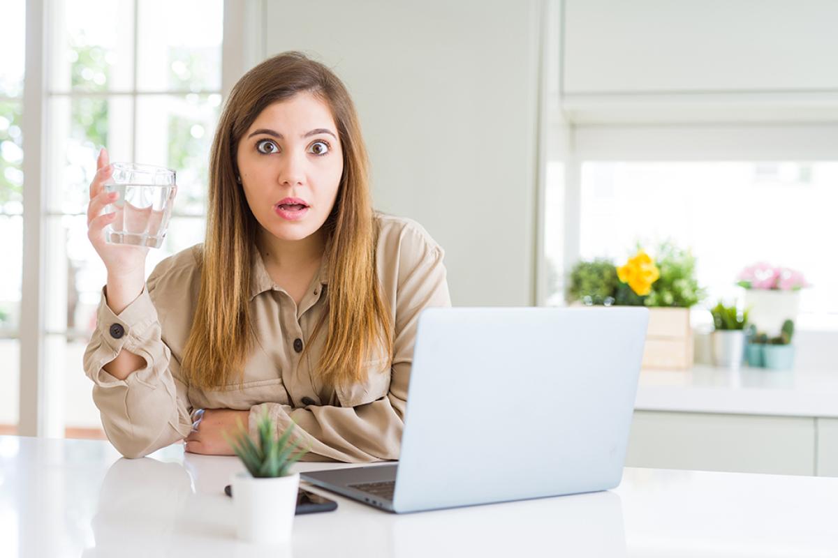 woman looking surprised holding a glass of water behind laptop